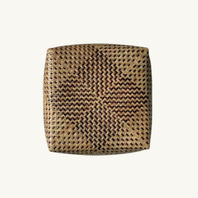 A square woven straw box or basket with rounded corners, featuring a tight zigzag pattern in natural tan and dark brown, centered on a solid off-white background.
