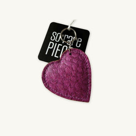A textured magenta purple fish leather heart-shaped keychain with a silver metal keyring and a black paper tag that reads 'SO RARE PIECEs' in white text, set against a plain off-white background.