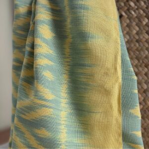 Handwoven Mudmee Ikat cotton scarf in lime yellow and soft green draped over bag