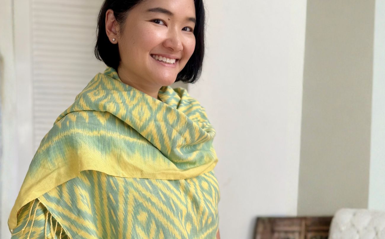 Smiling woman wearing a handwoven Ikat cotton scarf in lime yellow and soft green, Mudmee technique, handmade in Thailand, Whispered Patterns collection by So Rare Pieces